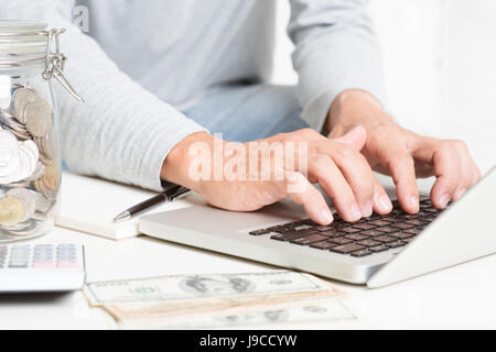 Mann tut, Online-Handel mit Laptop-Computer, Rechner, Tagebuch, Geld auf Tisch. Buchhaltung und Technologie. Stockfoto