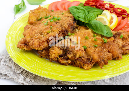 Schnitzel mit Gemüse, Tomatensauce auf weißem Holz Hintergrund. Nahaufnahme Stockfoto