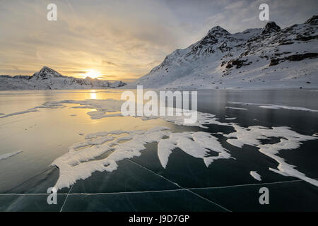 Die Eisfläche des Lago Bianco umrahmt von schneebedeckten Gipfeln im Morgengrauen, Berninapass, Kanton Graubünden, Engadin, Schweiz Stockfoto
