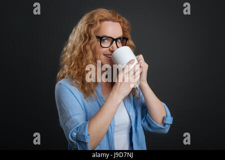Start in den Tag. Atemberaubende aktive hübsche Frau Heißgetränk aus einer Tasse trinken sie stehend auf grauem Hintergrund isoliert halten Stockfoto