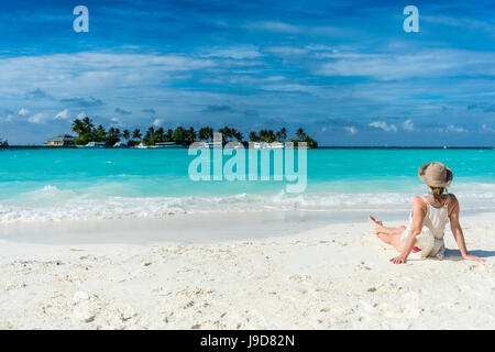 Frau sitzt auf einem weißen Sandstrand genießen das türkisfarbene Wasser, Sun Island Resort, Insel Nalaguraidhoo, Ari Atoll, Malediven Stockfoto