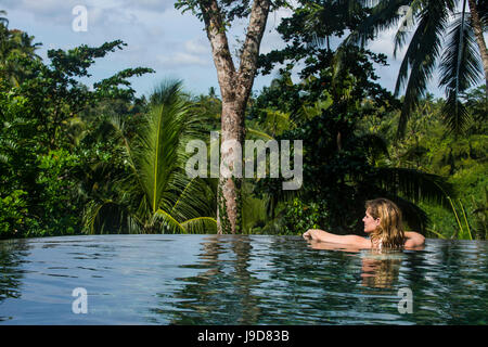 Frau genießen einen überlaufenden Pool über einem Tal im Kamandalu Ubud Resort, Ubud, Bali, Indonesien, Südostasien, Asien Stockfoto