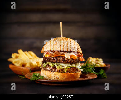 Big Beef-Burger mit Käse und Speck auf Holzplatte Stockfoto