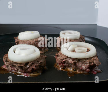 Vier Wild Burger braten garniert mit Zwiebelringen, in Antihaft-Pfanne auf einem Elektroherd, Nahaufnahme Stockfoto