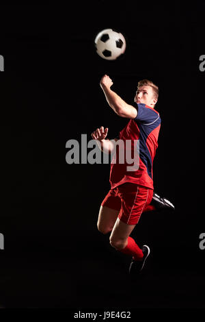 Profi-Fußballer springen, um Ball im Studio Kopf Stockfoto