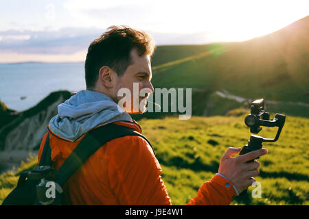 Attraktive junge Mann Filme ein Reisevideo mit dem DJI Osmo Mobile Steadycam Gimbal und ein Apple iPhone 7 auf Jurassic Coast, Dorset. Stockfoto