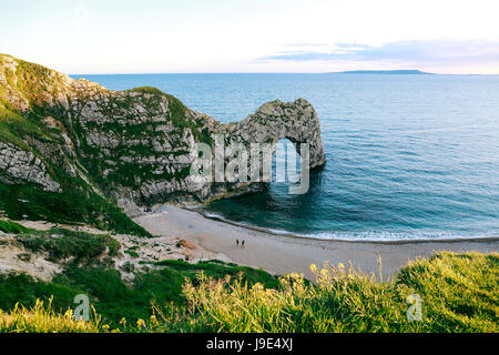 Blick vom Hügel über Menschen zu Fuß auf einem Strand am Meer und Durdle Door, einem natürlichem Kalkstein Bogen an Jurassic Küste von Dorset, UK Stockfoto