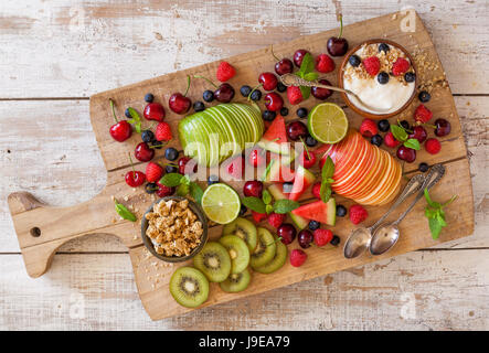 Obst und Joghurt zum Frühstück auf einem Holzbrett. Stockfoto