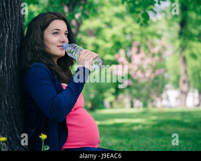 Schwangere Frau trinkt Wasser aus der Flasche im Freien. Kopieren Sie Raum. Stockfoto