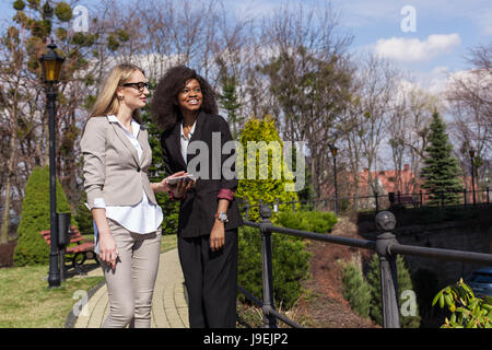 Eine schwarze und eine weiße Unternehmerinnen im Park spazieren und Gespräch. Stockfoto