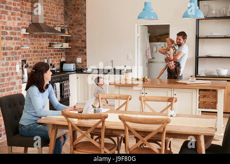 Vater spielt mit Kindern als Mutter arbeiten am Laptop Stockfoto