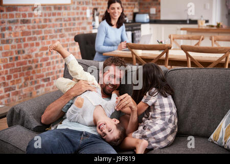 Vater spielt mit Kindern als Mutter arbeiten am Laptop Stockfoto