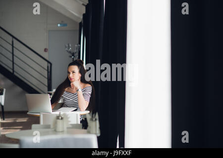 Auf der Suche nach Inspiration. Junge schöne nachdenkliche Frau einige Notizen machen und beim Sitzen im Stuhl an ihrem Arbeitsplatz wegsehen. Stockfoto
