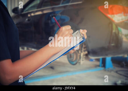 Asiatische Frauen Ingenieure und Techniker prüfen Mechaniker und Inspektion an einem Auto in der Autowerkstatt die Liste auf dem Brett Stockfoto