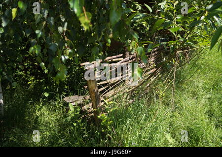 Hölzerne geflochtenen Zaun unter den Ästen ein grüner Baum auf dem Rasen an einem Sommertag Stockfoto