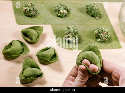 Grüne Tortelloni. Typische Bolognese hausgemachte frische Teigwaren im Vorbereitungsprozess zum Zeitpunkt der Schließung. Grüne Nudeln mit Flou geknetet Stockfoto