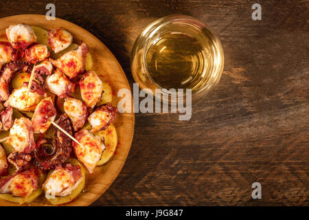 Eine obenliegende Foto von Pulpo a la Gallega, eine Krake mit gekochten Kartoffeln, typische spanische galizische Gericht, auf einer traditionellen hölzernen Platte, mit einem Glas-o Stockfoto