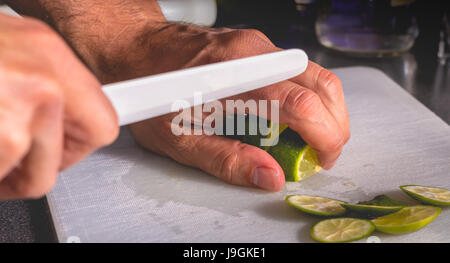 Barkeeper schneidet grüne Zitronen mit Keramikmesser, Caipirinha zu machen Stockfoto