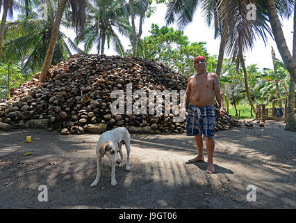 Miguel Córdoba steht mit seinem Hund vor seinem Stapel Kokosnussschalen, die er für Kokosöl aus der costaricanischen Karibik Stadt Pacua verkauft Stockfoto