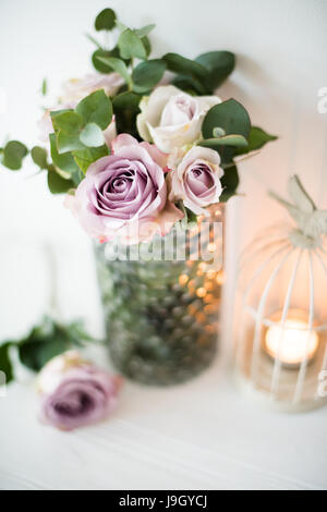 Pastell lila, lila Farbe frischen sommerlichen Rosen in Vase mit weißen Wand Hintergrund und Kerzen, Vintage-Stil Hochzeit Dekoration Stockfoto