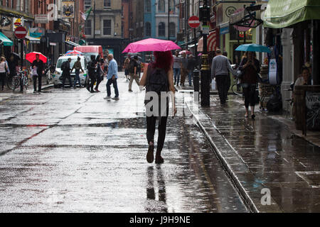 Soho, London, UK. 2. Juni 2017. Eine Frau Rosa Regenschirm ist von der Sonne beschienen, als es durch die Wolken bricht, gelangt nach einer der die Gewitter vorhergesagt durch das Met Office über Old Compton Street in Soho, London. Bildnachweis: Paul Davey/Alamy Live-Nachrichten Stockfoto