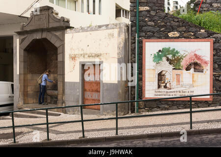 Ein Tourist Re-inszeniert eine Szene aus einer Reproduktion von ein Aquarell von Max Römer neben dem ursprünglichen Brunnen, die, den Sie in Funchal, Madeira aus gemalt wurde Stockfoto