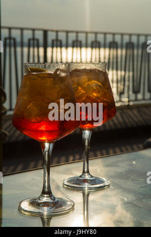 Kellner vorbereitet Aperol Sprits Sommer cocktail mit Aperol, prosecco, Eis-Würfel und Orange im Weinglas, bereit, auf der sonnigen Terrasse mit Meer zu trinken Stockfoto