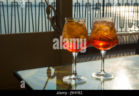 Kellner vorbereitet Aperol Sprits Sommer cocktail mit Aperol, prosecco, Eis-Würfel und Orange im Weinglas, bereit, auf der sonnigen Terrasse mit Meer zu trinken Stockfoto