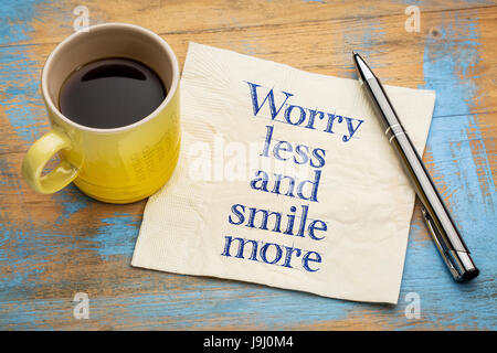 Sorgen Sie weniger und mehr - Lächeln Sie Handschrift auf einer Serviette mit einer Tasse Espressokaffee Stockfoto