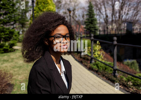 Porträt von schönen schwarzen Geschäftsfrau im Park. Frau mit Brille und hat dunkle locken. Stockfoto