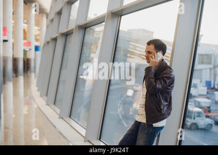 Porträt eines schönen Jugendlichen casual-Style Kleidung stehen in der Nähe von Fenster in modernen Flughafenterminal. Reisende mit Smartphone Anruf tätigen. Stockfoto