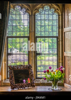 Hever Castle, England - April 2017: Kleine gravierte Spiegel und bunte Tulpen in einer Vase auf einer Fensterbank in einem alten Gebäude Stockfoto