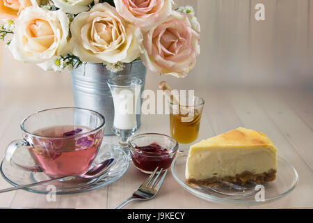 Vase Bouquet Rosen in Aluminium Schaufel mit blueberry Cheesecake und Aroma rose Tee mit Honig, Kaffee Pause, auf Holztisch, set Schöne Blume Stockfoto