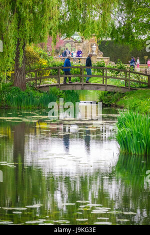 Hever Castle, England - April 2017: Ältere Menschen zu Fuß über die kleine Holzbrücke im Hever Schlossgarten, Kent, England, UK Stockfoto