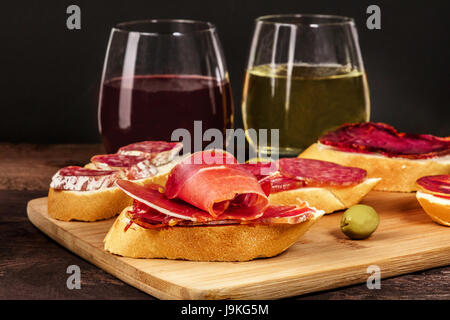 Ein Foto von Montsà Tapas, sandwiches mit Schinken, Salchichon, Lomo und andere spanische Würste, mit Gläsern Wein und grüne Oliven auf einen dunklen Rücken Stockfoto