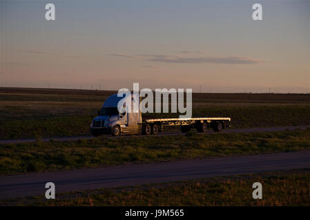 Ein weiß oder Silber Freightliner Semi-LKW zieht eine leere Flachbett Auflieger entlang einer ländlichen uns Interstate am späten Nachmittag. Stockfoto