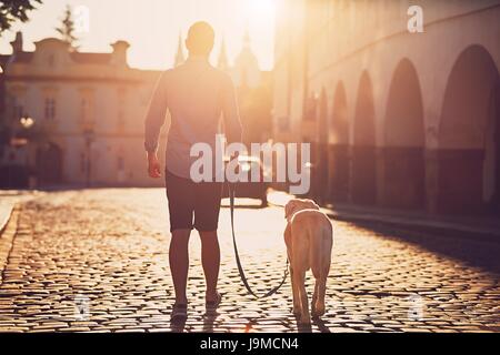 Morgen in der Stadt. Junger Mann mit seinem Hund auf der alten Straße bei golden Sunrise laufen. Prag, Tschechische Republik Stockfoto