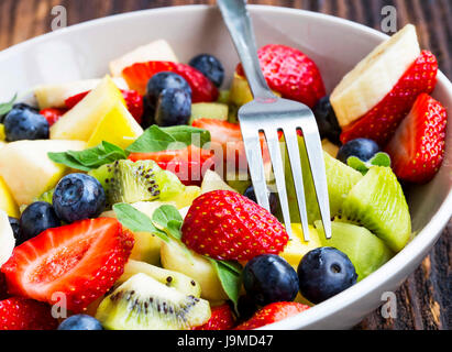 Salat von frischen Früchten und Gabel in einer Schüssel mit Erdbeeren, Kiwi, Banananas, Blaubeeren, Äpfel Stockfoto