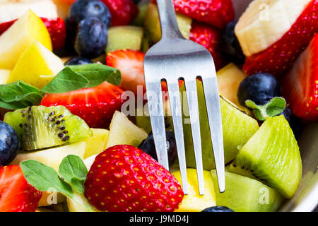 Salat von frischen Früchten und Gabel in einer Schüssel mit Erdbeeren, Kiwi, Banananas, Blaubeeren, Äpfel Stockfoto