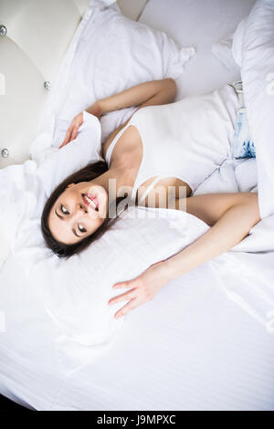 Schönen Tag-Träumer. Draufsicht der schönen jungen Frau, die Hand in Hand hinter Kissen im Bett liegend und lächelnd Stockfoto