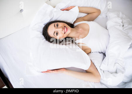Schönen Tag-Träumer. Draufsicht der schönen jungen Frau, die Hand in Hand hinter Kissen im Bett liegend und lächelnd Stockfoto