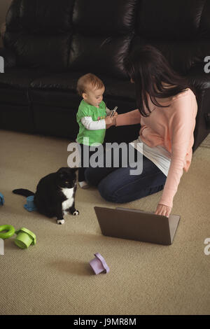 Mutter mit Laptop und betrachten ihre Tochter Holding Handy im Wohnzimmer Stockfoto