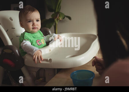 Baby betrachten ihrer Mutter beim Sitzen im Hochstuhl zu Hause Stockfoto
