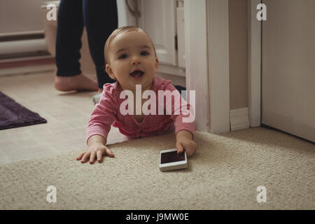 Porträt von lächelndes Babymädchen mit Handy auf Boden zu Hause Stockfoto