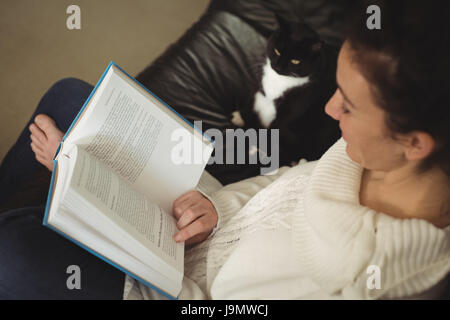Frau liest Roman während Katze sitzt neben zu Hause auf sofa Stockfoto
