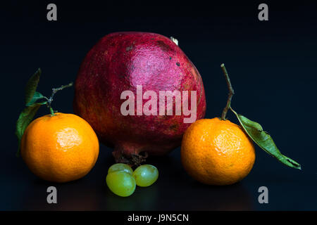 Mandarinen, Granatapfel und Trauben auf schwarzem Hintergrund Stockfoto