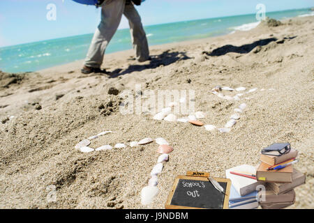 Konzept des Sommers und der Schule Ende mit dem Wort Meer mit Muscheln auf Sand und ein paar Bücher gemacht Stockfoto