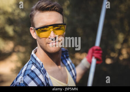 Porträt von gut aussehender Mann tragen Brillen mit Oliven Rake auf Bauernhof Stockfoto