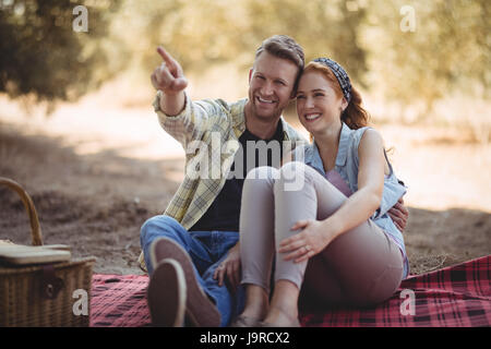 Lächelnd jungen Mann zeigt etwas zu Frau beim Sitzen am Olivenfarm Stockfoto