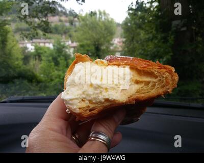 Frau hält köstliche Delikatesse der Brioche mit Vanillesauce. Kuchen zu Essen an der frischen Luft ist sehr gut. Stockfoto